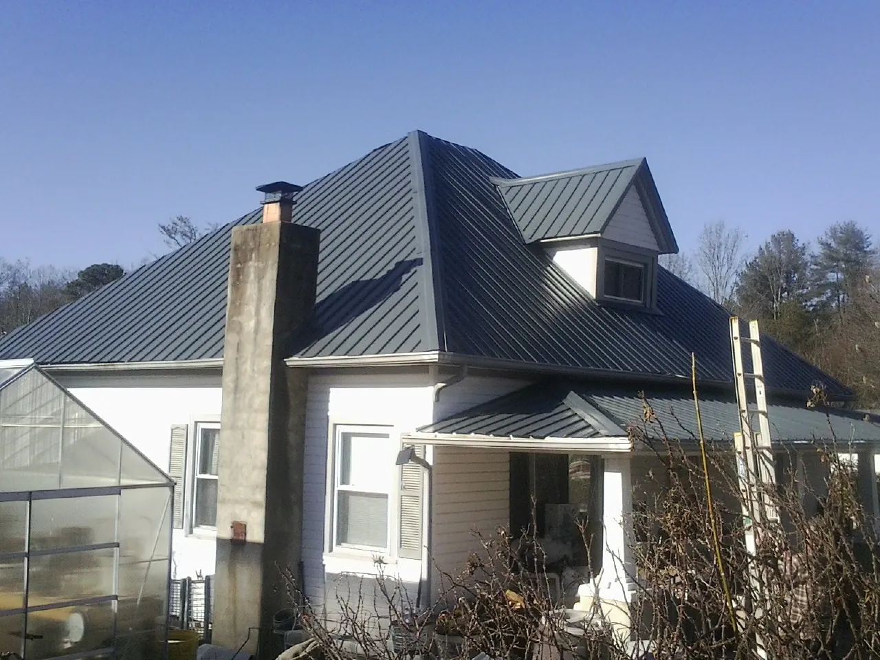 Dark blue standing seam metal roof on a white farmhouse with dormer — Slate & Tile Roof Repair by Roofing Brothers in Caruthers