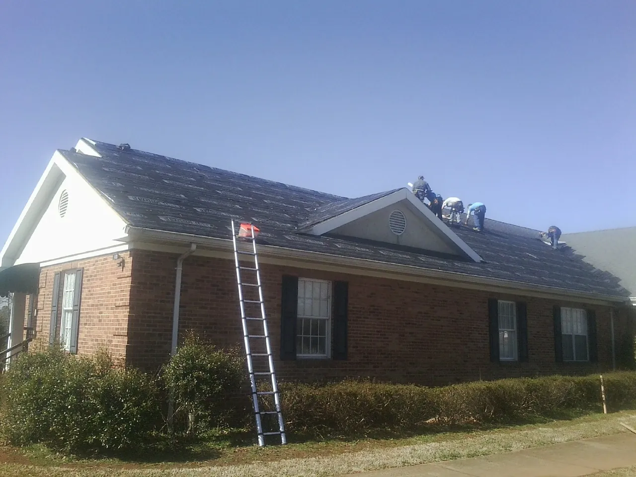 Crew tearing shingles off a brick ranch roof with a ladder set — Metal Roof Repair work by our crew in Caruthers