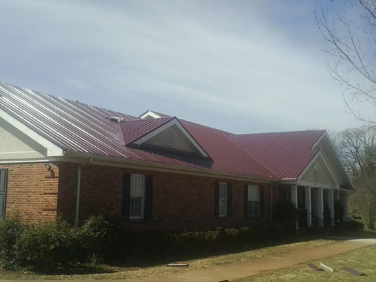 Red metal roof with gabled entries on a long brick building, from a Hail Damage Roof Repair job in Caruthers
