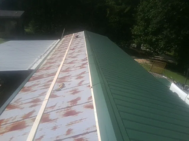 Old rusted panels beside newly installed green metal roofing — Wind Damage Roof Repair by Roofing Brothers in Caruthers