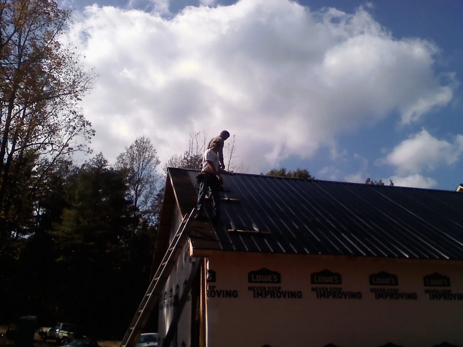 Roofer fastening dark metal panels high against a cloudy sky, from a Roof Inspection job in Caruthers