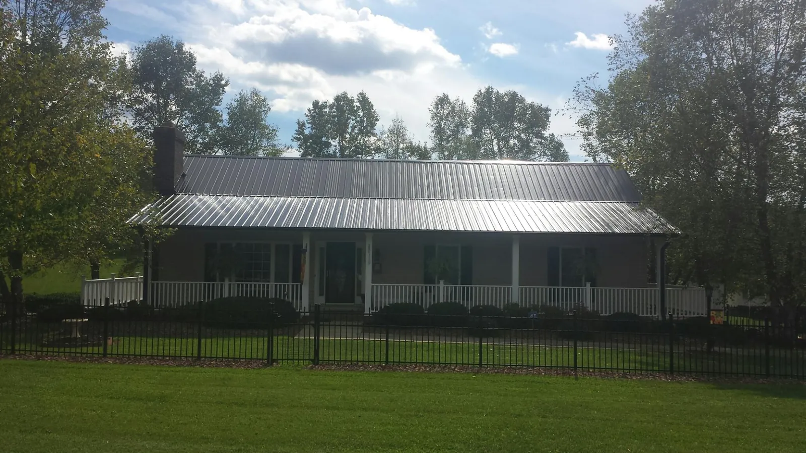 Gray metal roof on a brick ranch with a full width front porch — Gutter Guard Installation work by our crew in Caruthers