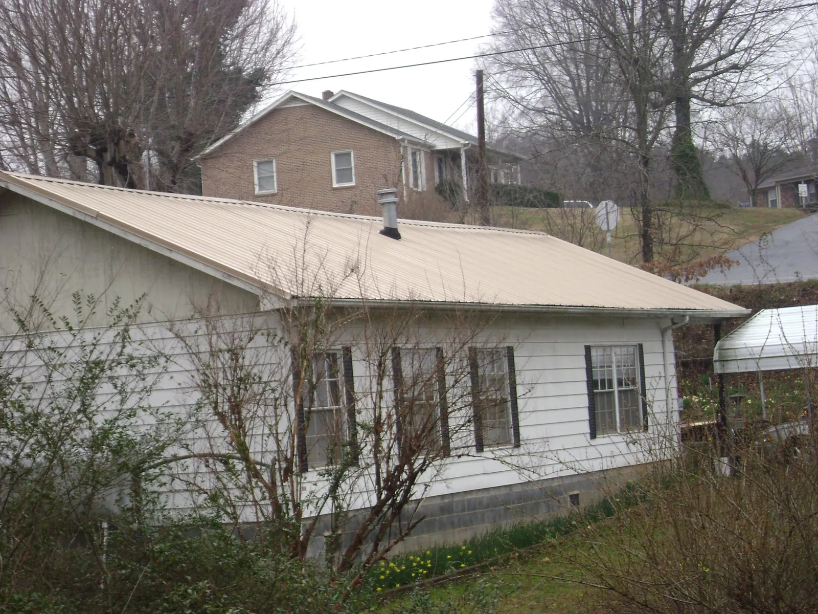 Tan metal roof on a white sided house set into a hillside — Commercial Roofing by Roofing Brothers in Caruthers