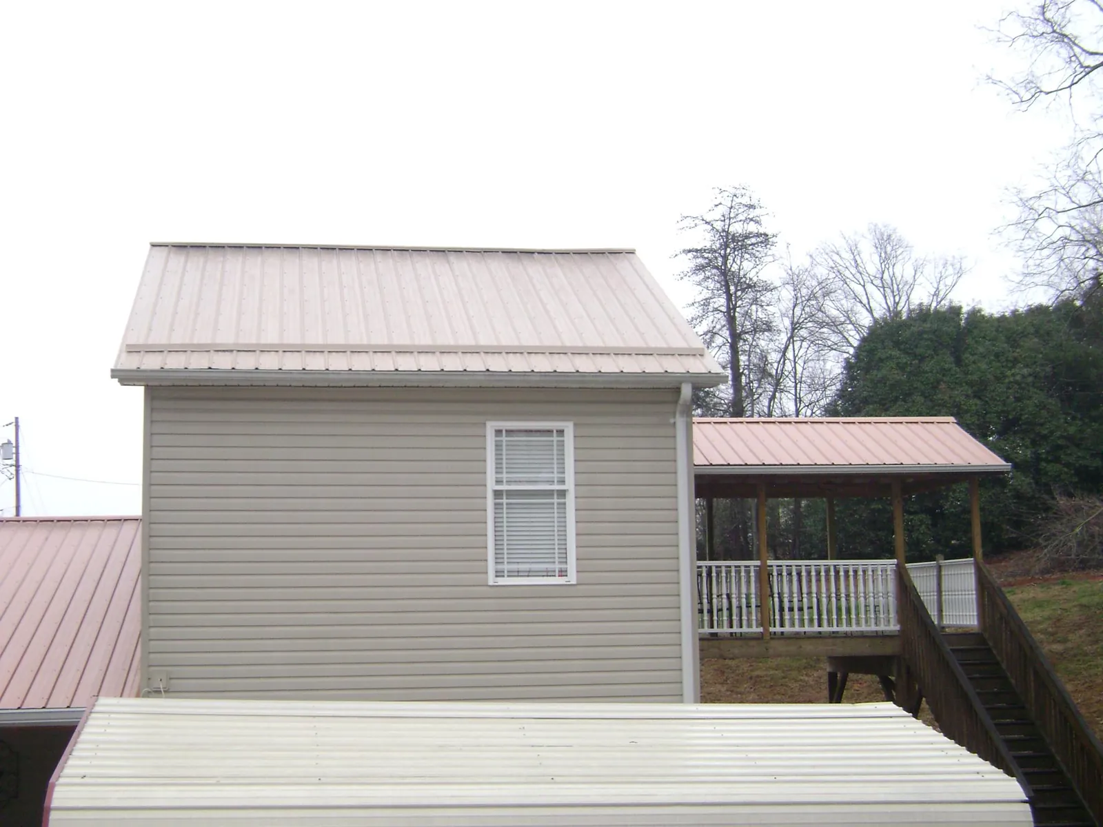Tan metal roofs on a two story addition and attached porch, from a Roof Replacement job in Caruthers
